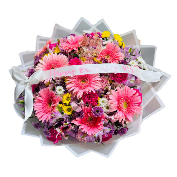 Round birthday bouquet of pink gerbera daisies and mixed flowers with a ribbon and small crown decoration