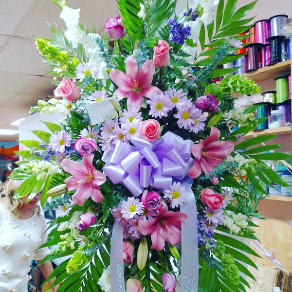 Large floral standing spray with pink lilies, roses, and daisies, tied with a lavender bow
