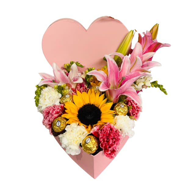 Heart-shaped pink box with pink lilies, carnations, a sunflower, and gold-wrapped chocolates