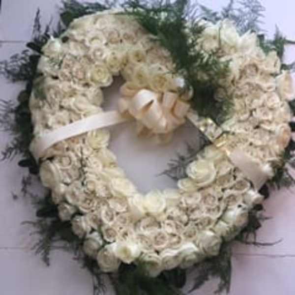 White floral wreath with a ribbon bow and dark greenery
