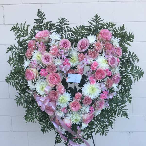 Heart-shaped pink and white floral wreath on a stand with ribbon