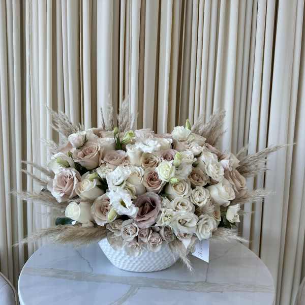Blush and ivory rose arrangement in a white vase with pampas grass
