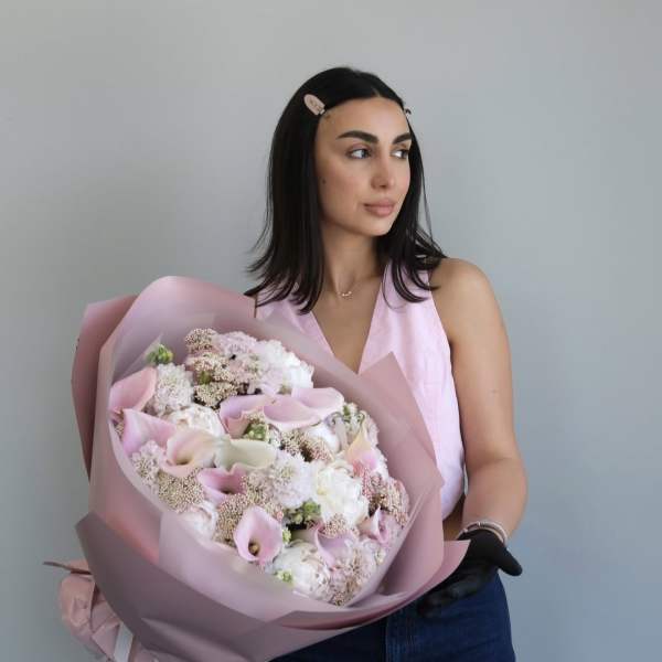 Woman holding a large bouquet of pale pink and white flowers wrapped in pink paper
