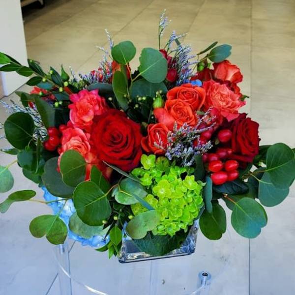 Low arrangement of red and coral roses with green hydrangea in a square glass vase