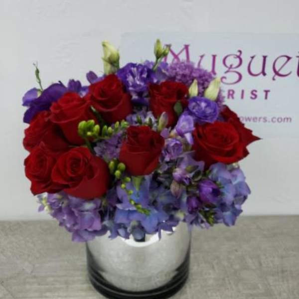 Red roses and purple flowers arranged in a silver vase