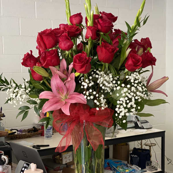 Tall bouquet of red roses and pink lilies in a clear glass vase