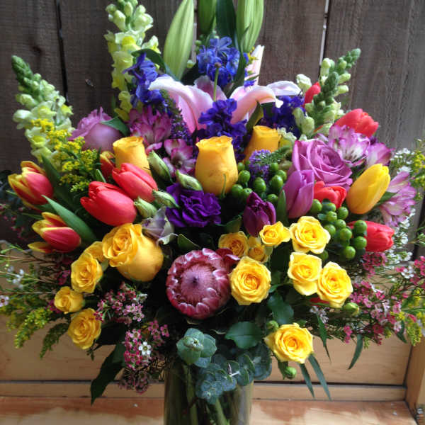 Colorful mixed bouquet in a clear glass vase with roses, tulips, lilies, and snapdragons