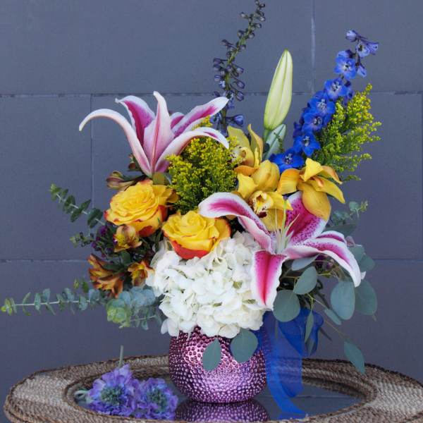 Mixed bouquet with lilies, roses, hydrangea, and blue delphinium in a pink vase