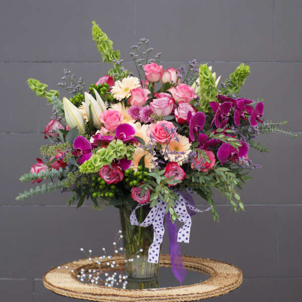 Mixed bouquet of pink roses, orchids, and lilies in a glass vase