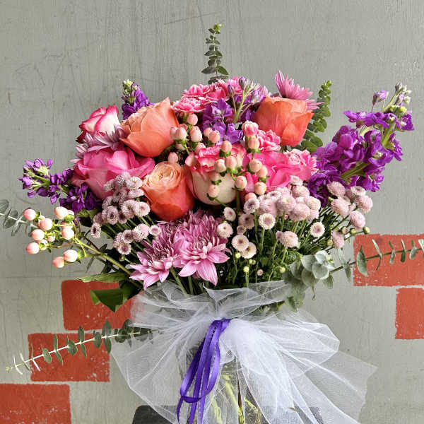 Pink and purple mixed bouquet in a glass vase with a white tulle bow