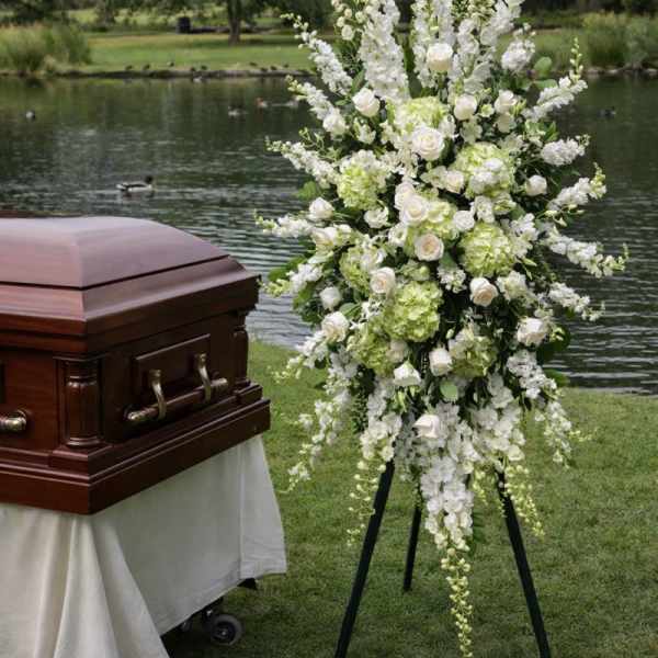 White funeral spray beside a casket outdoors by a lake