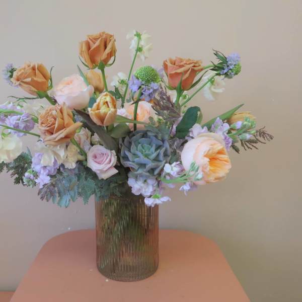 Peach roses and lavender flowers in a ribbed glass vase