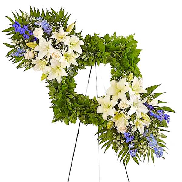 Heart-shaped floral wreath with white lilies and blue flowers on a stand