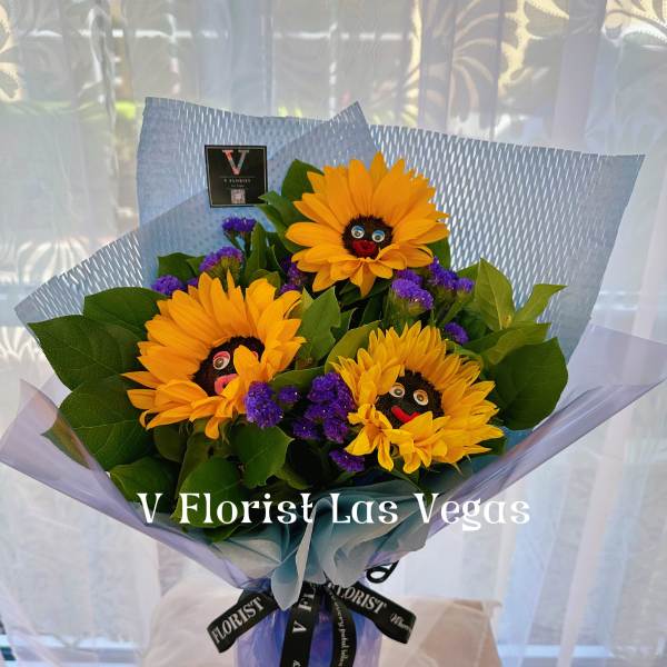 Hand-tied bouquet of yellow sunflowers with purple accents in blue wrap on a stand