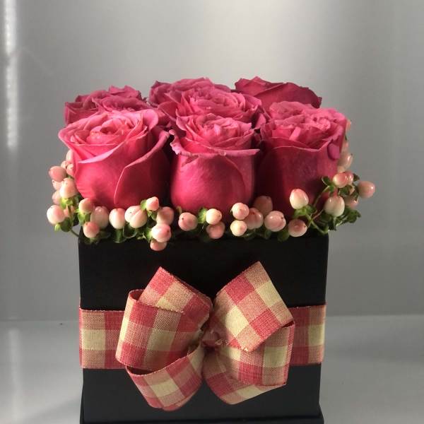 Pink roses arranged in a black box with a plaid ribbon bow