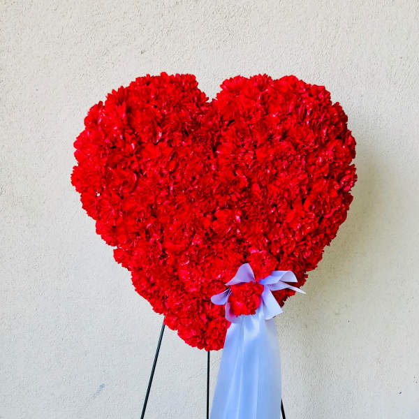 Heart-shaped red floral arrangement on a stand with a pale ribbon