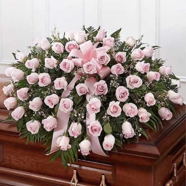 Pink rose casket spray with ribbon on a wooden coffin