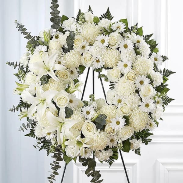White floral wreath on a black stand with roses, daisies, and lilies