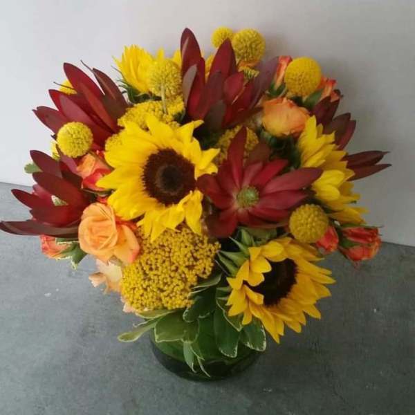 Bouquet of sunflowers, red blooms, and peach roses in a glass vase