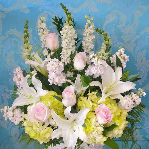 Basket arrangement of white lilies, pink roses, and pale hydrangeas