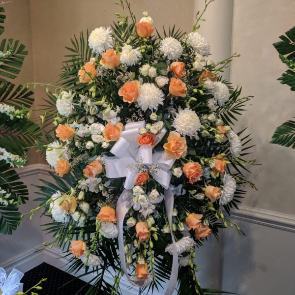 Large standing floral spray with peach roses and white blooms on a ribboned easel