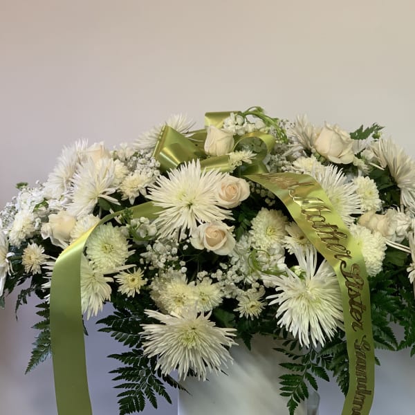 White floral casket spray with green ribbon and fern accents