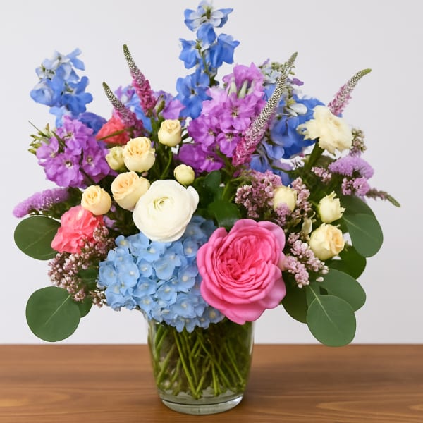 Mixed bouquet of blue, pink, and cream flowers in a clear glass vase
