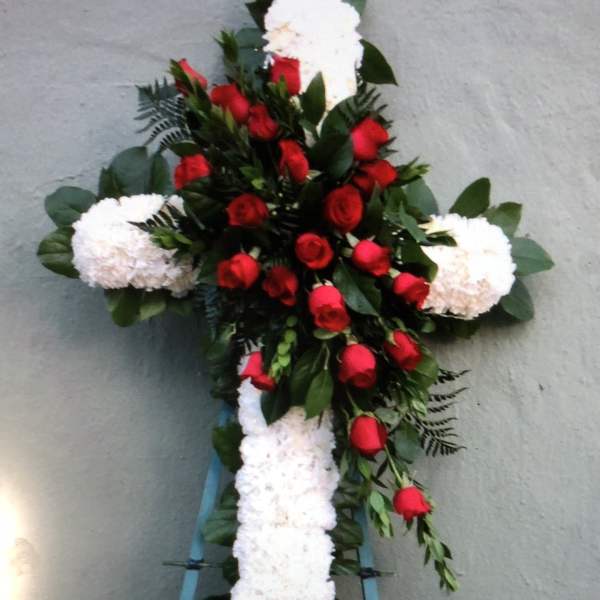 Cross-shaped floral tribute with red roses and white flowers on a stand