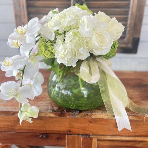 White orchid and rose arrangement in a green glass vase with ribbon