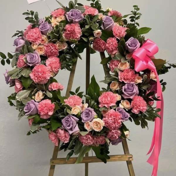 Standing wreath of pink carnations and lavender roses with a pink bow on a wooden easel