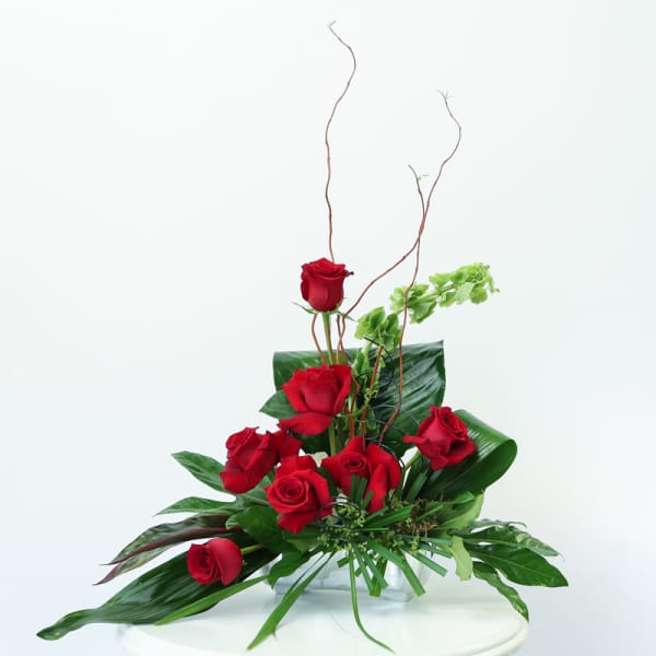 Red roses arranged in a clear glass vase with tall curly branches