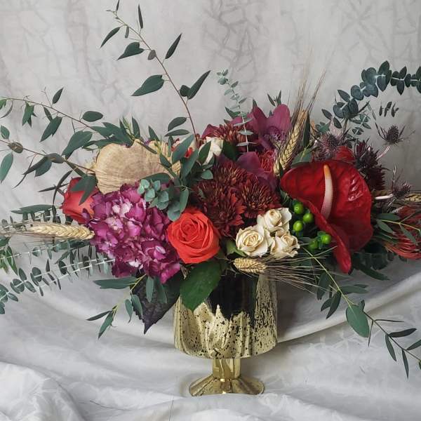 Mixed floral arrangement in a gold vase with red and pink blooms