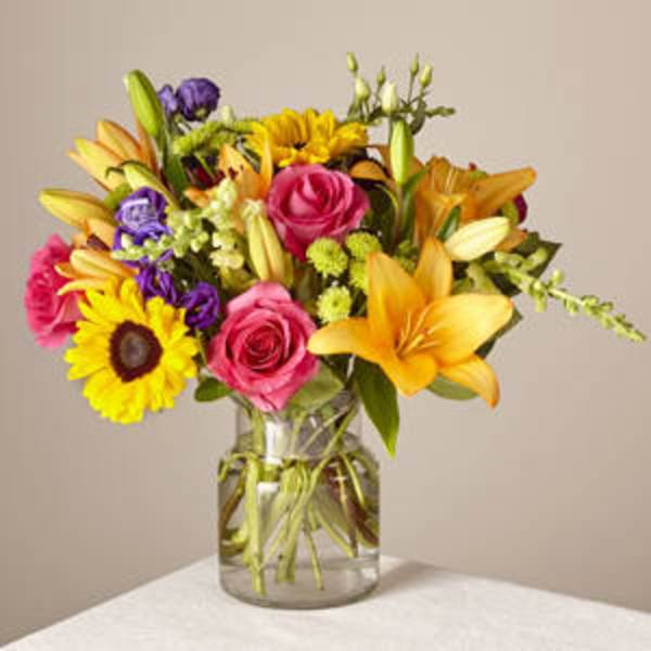 Mixed bouquet of roses, lilies, and sunflowers in a glass vase