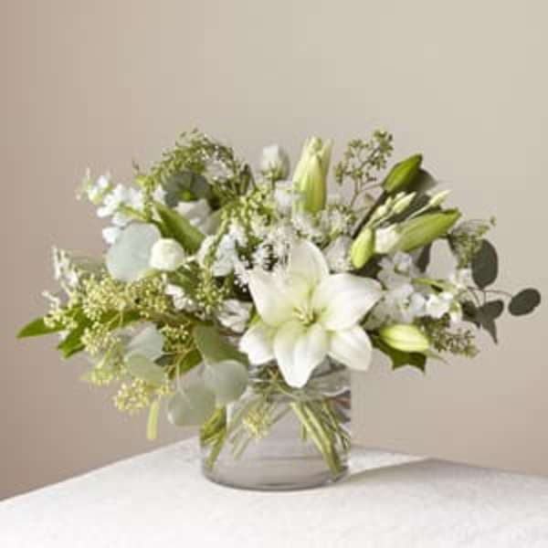 White lilies and small white flowers in a clear glass vase