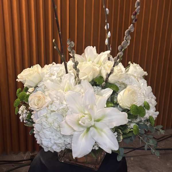 White floral arrangement in a square glass vase with roses and lilies