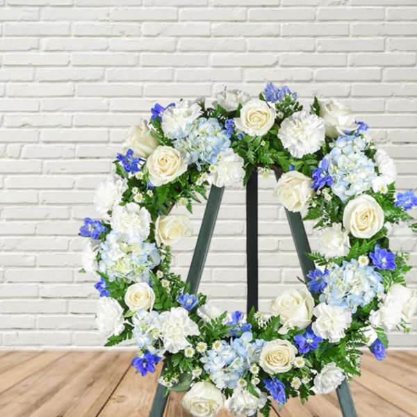 Floral wreath with white roses, blue hydrangeas, and white blooms on an easel