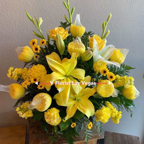 Tall yellow floral arrangement with lilies, roses, and daisies in a container