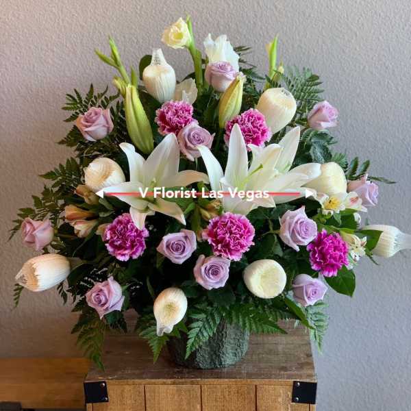 Tall arrangement of white lilies, pink carnations, and lavender roses in a green vase