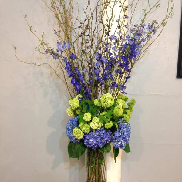 Tall blue and green floral arrangement in a clear glass vase