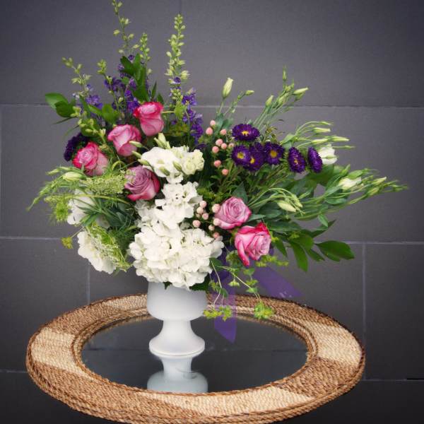 Pink and white floral arrangement in a white pedestal vase