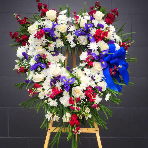 Large floral wreath with white roses, purple irises, and red accents on an easel