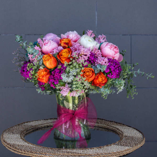 Pink and orange mixed bouquet in a glass vase with a magenta ribbon