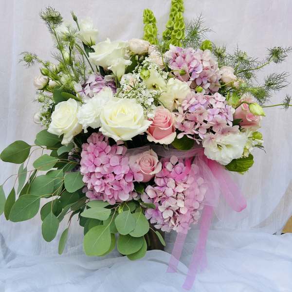 Bouquet of pink and white roses with hydrangeas and greenery, tied with pink ribbon