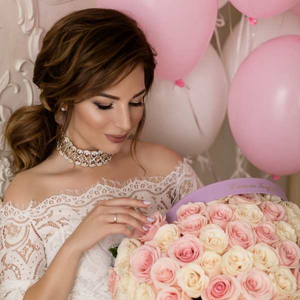 Woman in lace dress holding a lavender hat box filled with pink and cream roses