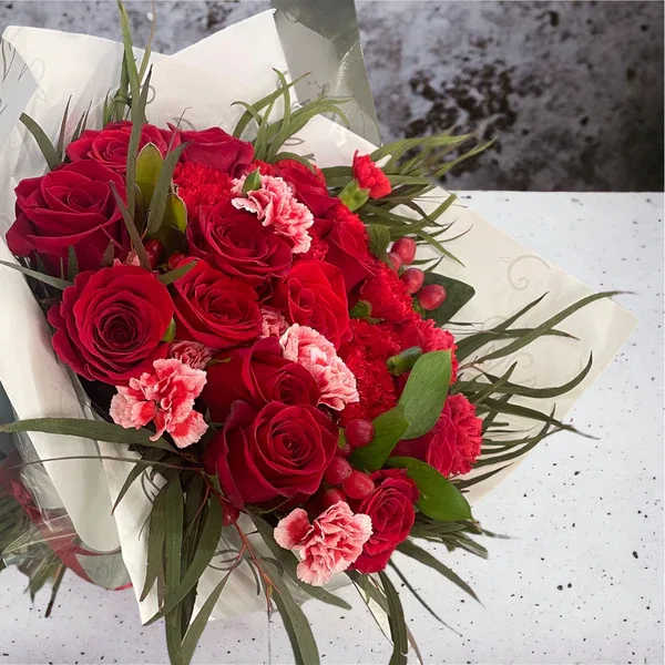 Bouquet of red roses and pink carnations wrapped in white paper