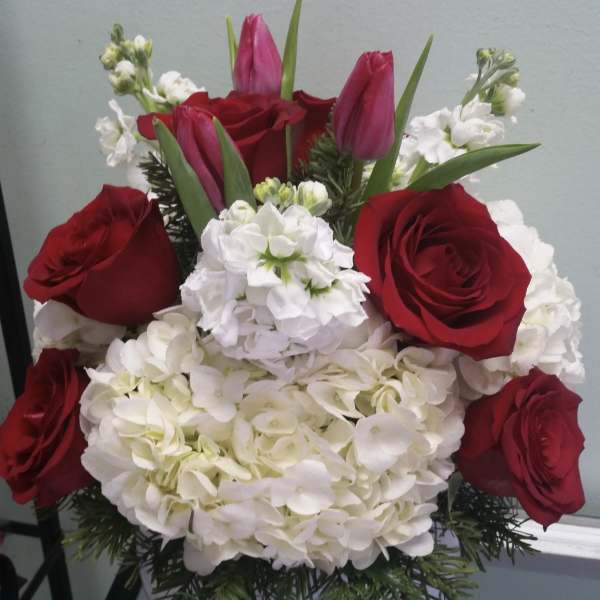 Red roses and pink tulips arranged with white hydrangeas in a vase