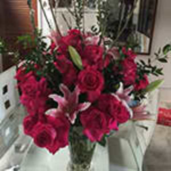 Tall arrangement of red roses and pink lilies in a clear glass vase