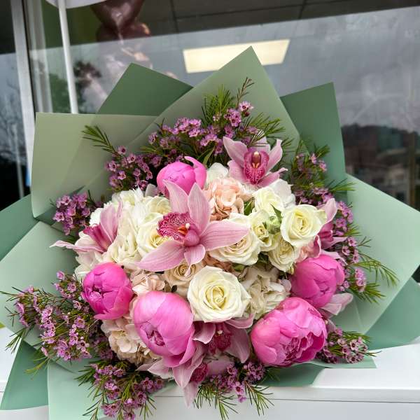 Bouquet of pink peonies, orchids, and white roses wrapped in green paper
