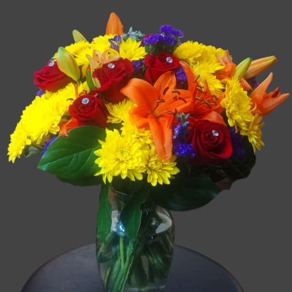 Bouquet of red roses, orange lilies, and yellow mums in a glass vase