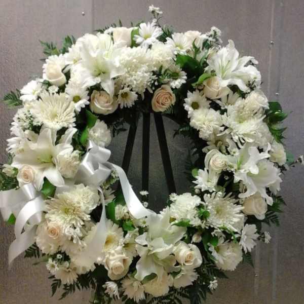White floral wreath on a black easel with a ribbon bow
